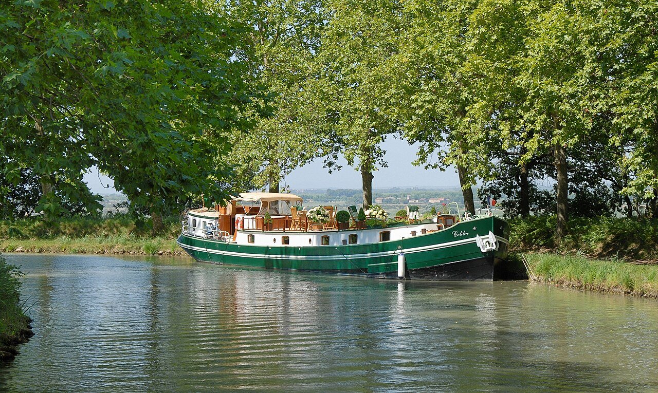 Bateau habitable fluvial naviguant sur un canal calme bordé d'arbres